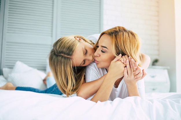 Linda jovem mãe bonita está abraçando sua linda filha. Mãe e menina deitadas na cama branca e relaxando juntos e se divertindo e passando tempo juntos