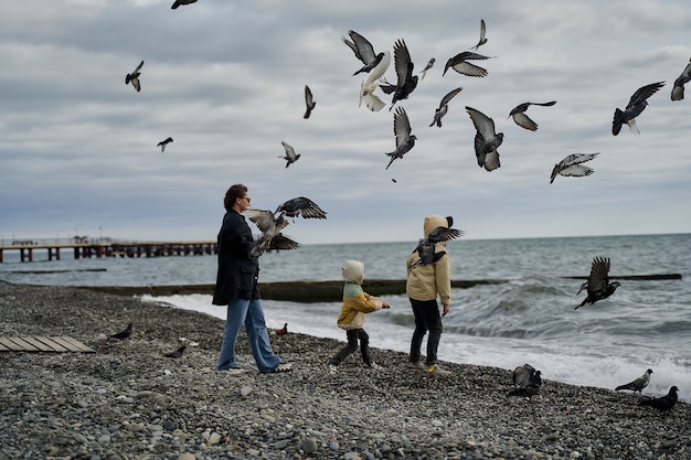 Foto linda jovem mãe com filhos na costa do mar e pombos.