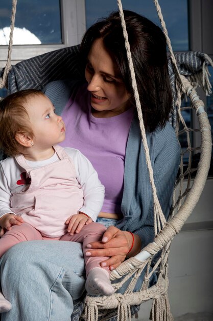 Linda jovem mãe com sua filha bonita e feliz em uma cadeira de balanço pendurada.