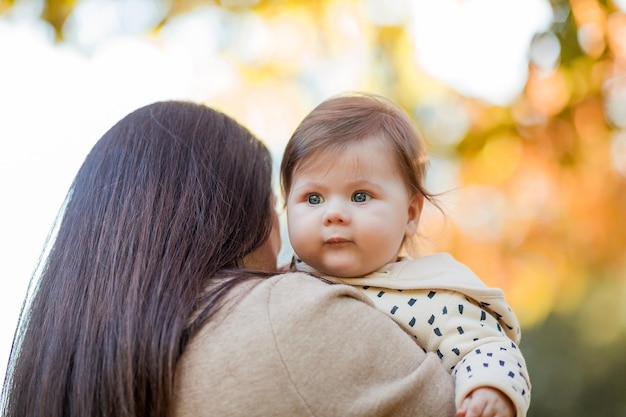 Linda jovem mãe com uma linda garotinha de 7 meses caminha no parque de outono Retrato de uma família feliz Queda