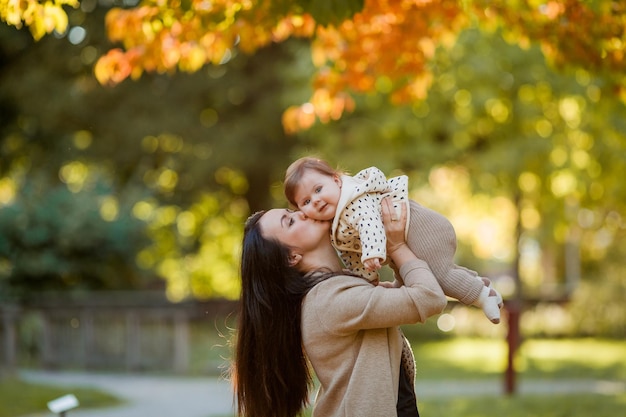 Linda jovem mãe com uma linda garotinha de 7 meses caminha no parque de outono Retrato de uma família feliz Queda