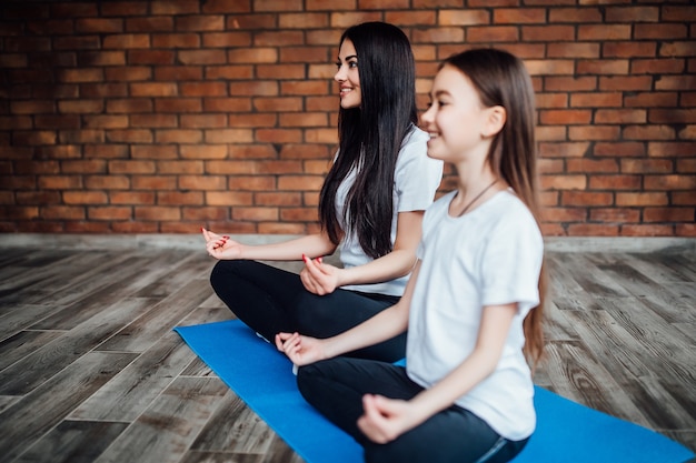 Linda jovem mãe e adorável filha durante o exercício no tapete azul.