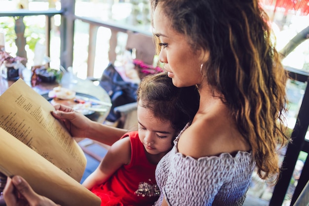 Linda jovem mãe e filha bonitinha bochechando menu no café