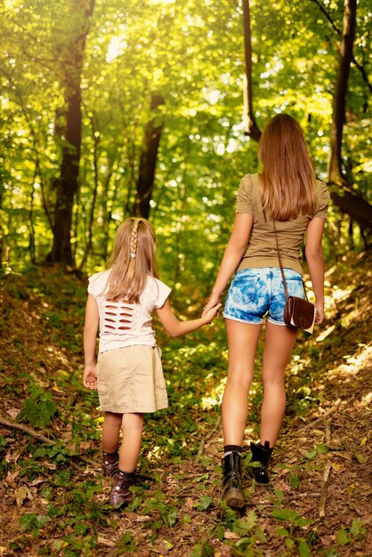 Linda jovem mãe e sua filha andando pela floresta. Visão traseira.