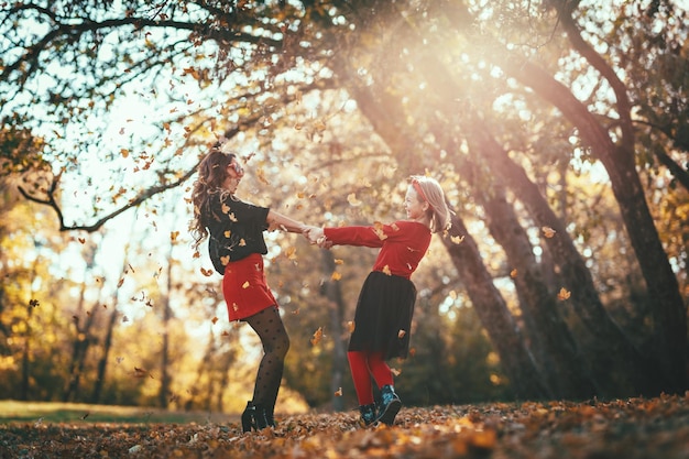 Linda jovem mãe e sua filha feliz estão se divertindo na floresta ao pôr do sol. Eles estão de mãos dadas, rindo e se virando.