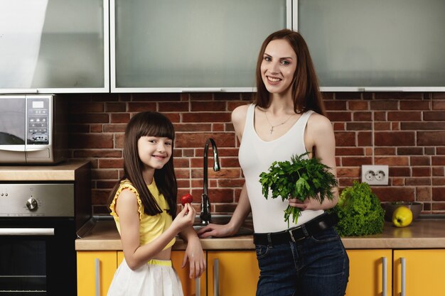 Linda jovem mãe e sua linda filha em pé na cozinha