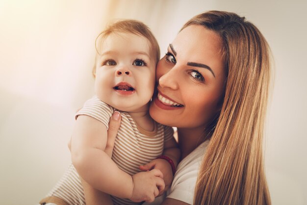 Linda jovem mãe se divertindo com seu bebê fofo em casa. Olhando para a câmera