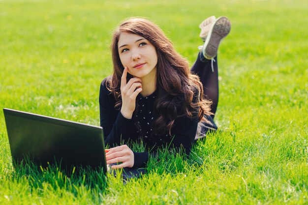 Linda jovem, menina da escola usando laptop no parque deitado na grama verde. o conceito de tempo de lazer. conceito de e-learning.