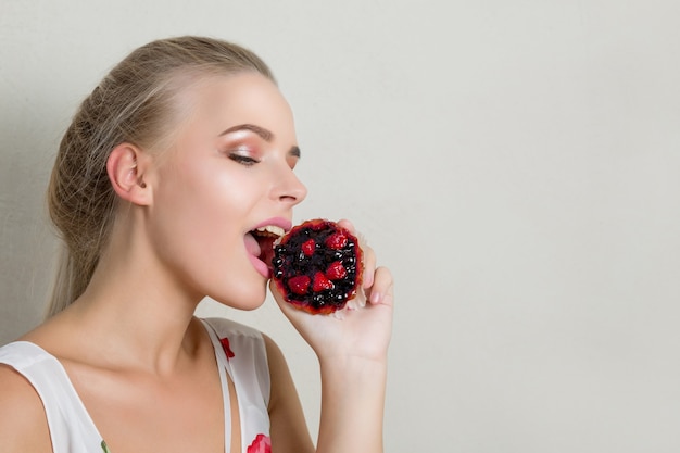 Foto linda jovem modelo loira mordendo um bolinho doce com frutas. espaço para texto
