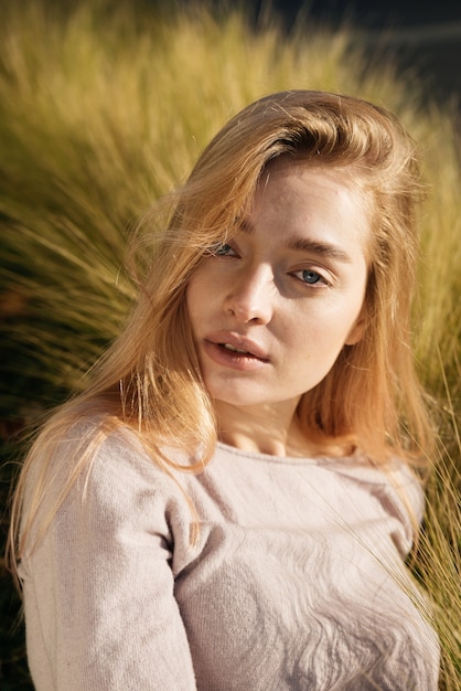 Linda jovem modelo loira sentada na grama ao sol e poses