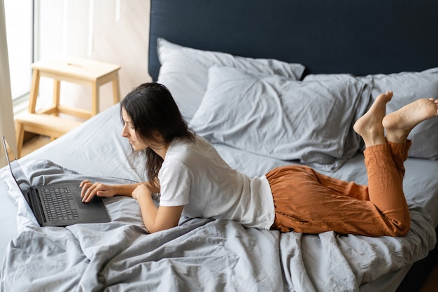 Linda jovem morena com um laptop deitado na cama