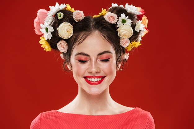 Linda jovem morena com um penteado floral incrível usando maquiagem posando isolada na parede vermelha