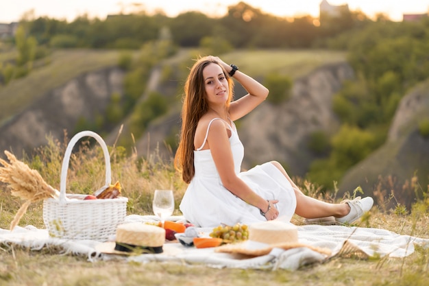 Linda jovem morena com um vestido branco, fazendo um piquenique em um lugar pitoresco. Piquenique romântico