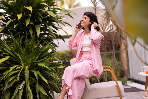 Linda jovem morena europeia sorrindo falando no telefone sentado no terraço no jardim verde conceito de comunicação por telefone