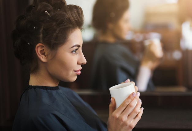 Linda jovem morena tomando uma xícara de café no salão de beleza