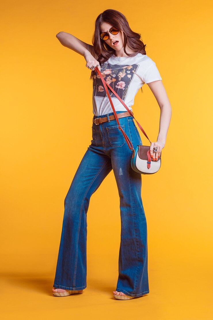 Foto linda jovem morena vestindo jeans t-shirt branca queimada com uma pequena bolsa de pé sobre um fundo amarelo no estúdio. visual brilhante e elegante