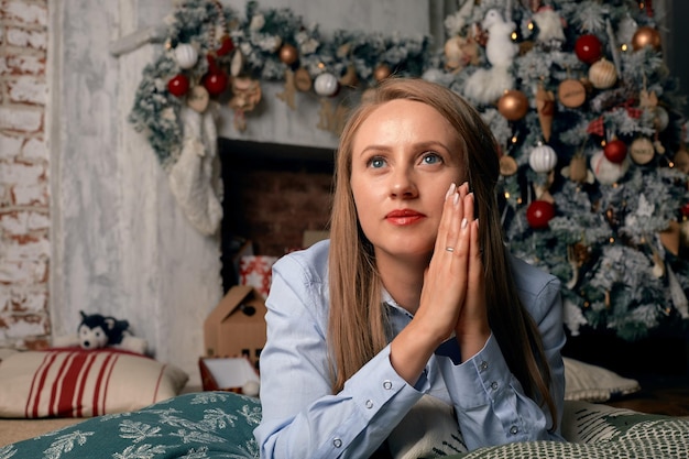 Linda jovem na véspera do natal está em frente a uma lareira com uma árvore de natal