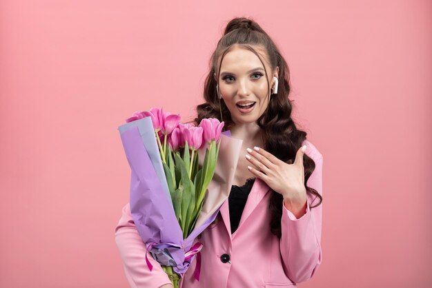 Linda jovem recebendo animadamente um buquê de tulipas para o dia das mulheres em fundo rosa