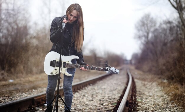 Linda jovem roqueira com guitarra elétrica Uma garota músico de rock em uma jaqueta de couro com uma guitarra canta Um solista de banda de rock toca guitarra e grita no microfone