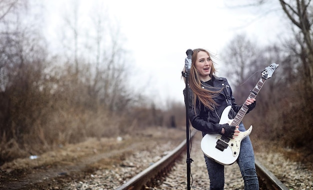 Linda jovem roqueiro com guitarra elétrica Uma garota músico de rock em uma jaqueta de couro com uma guitarra canta Um solista de banda de rock toca guitarra e grita no microfonexA