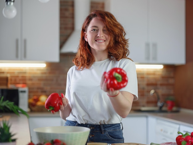 Linda jovem ruiva está preparando salada de legumes na cozinha