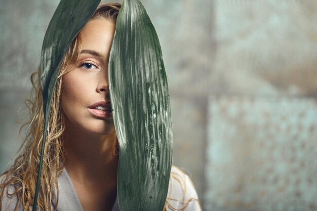 Linda jovem segurando grandes folhas verdes tropicais nas mãos e cobre parte do rosto