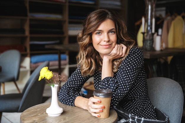 Linda jovem sentada em um café dentro de casa, bebendo café