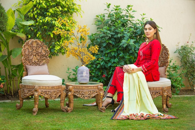 Linda jovem sentada sozinha no sofá no jardim usando vestido vermelho