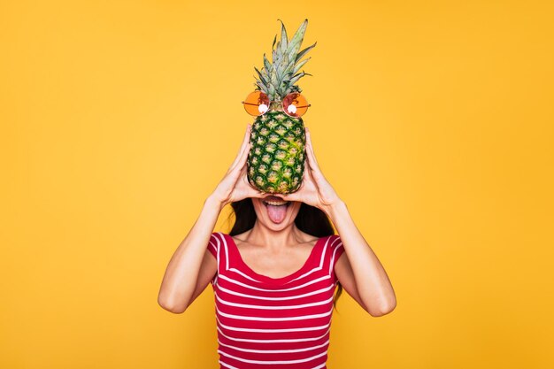 Linda jovem sorridente com abacaxi nas mãos em fundo laranja Frutas tropicais Alimentação saudável