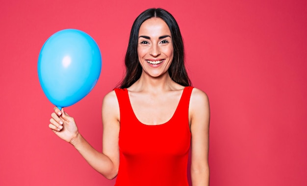 Linda jovem sorridente com balão azul na mão menina olha na câmera sobre fundo rosa