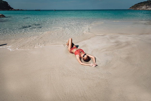 linda jovem tomando banho de sol na praia em um maiô vermelho