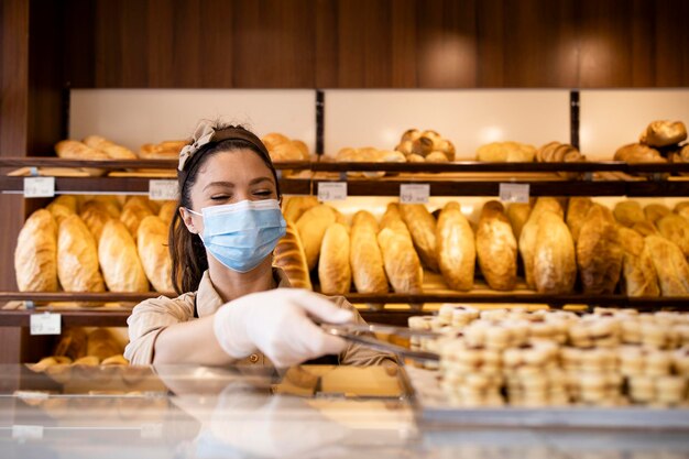 Linda jovem trabalhadora com máscara protetora trabalhando na padaria