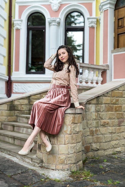 Linda jovem usa um pano elegante em pé perto de um prédio da cidade