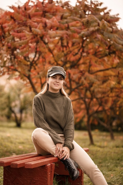 Linda jovem vestida com roupas elegantes, suéter verde e calça bege, em um parque de outono com lindas árvores