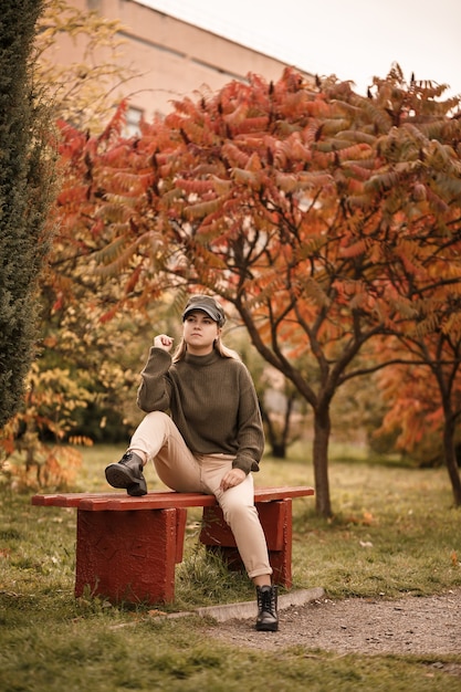 Linda jovem vestida com roupas elegantes, suéter verde e calça bege, em um parque de outono com lindas árvores