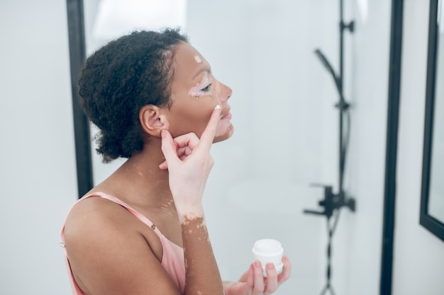 Una linda joven aplicando crema hidratante en su rostro