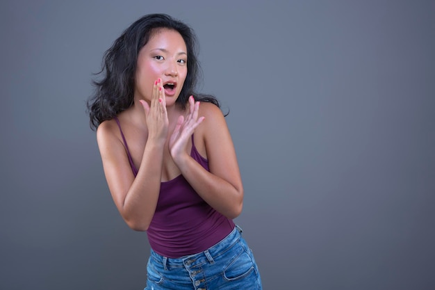 Linda joven asiática en camiseta sin mangas con expresión divertida aislada del fondo