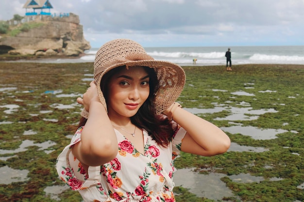 Una linda joven asiática que lleva un sombrero para el sol se relaja en la playa azul del cielo en Gunungkidul Indonesia