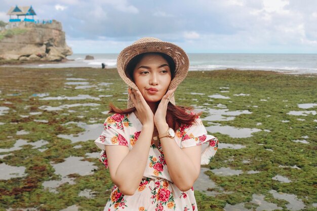 Una linda joven asiática que lleva un sombrero para el sol se relaja en la playa azul del cielo en Gunungkidul Indonesia