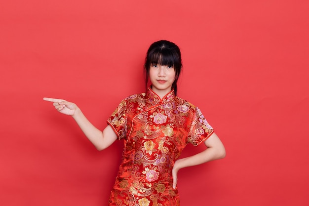 Linda joven asiática usar cheongsam apuntando al vacío para el concepto de año nuevo chino en un rojo