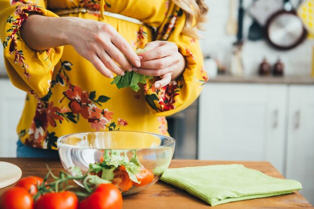 Linda joven embarazada preparando ensalada de verduras en la cocina