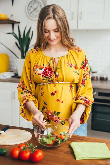 Linda joven embarazada preparando ensalada de verduras en la cocina