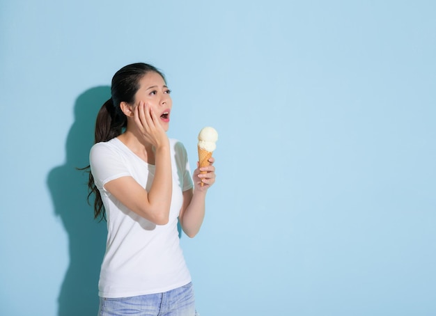 linda joven estudiante comiendo helado sintiendo dolor en los dientes y descubrió que tenía un problema dental sensible, mire el área vacía de fondo azul y quiere obtener ayuda.