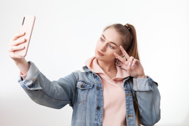 Linda joven estudiante hace selfie en smartphone aislado sobre fondo blanco.