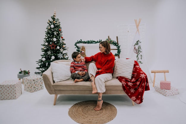 Linda joven familia riéndose sentada en el sofá en casa cerca del árbol de Navidad