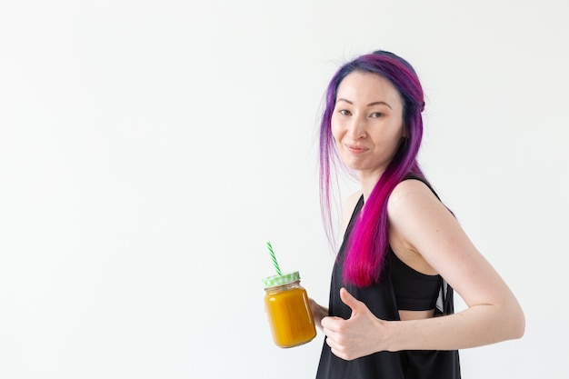 Linda joven inconformista de raza mixta con cabello teñido bebe batido de frutas antes de comenzar una clase de yoga sobre un fondo blanco con espacio de copia. Concepto de estilo de vida saludable. Copyspase.