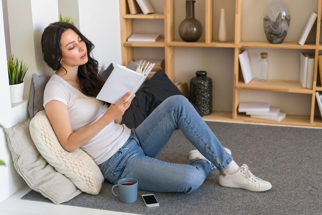 Linda joven leyendo un libro mientras está sentado en casa un fin de semana.