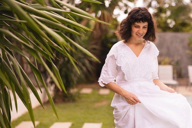 Linda joven morena caucásica sosteniendo falda de vestido blanco camina al aire libre mirando sus pies