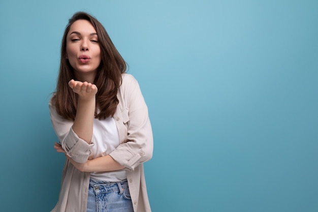 Una linda joven morena con un estilo elegante envía un beso en un fondo azul con espacio para copiar