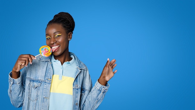 Linda joven negra lamiendo piruleta mostrando espacio de copia